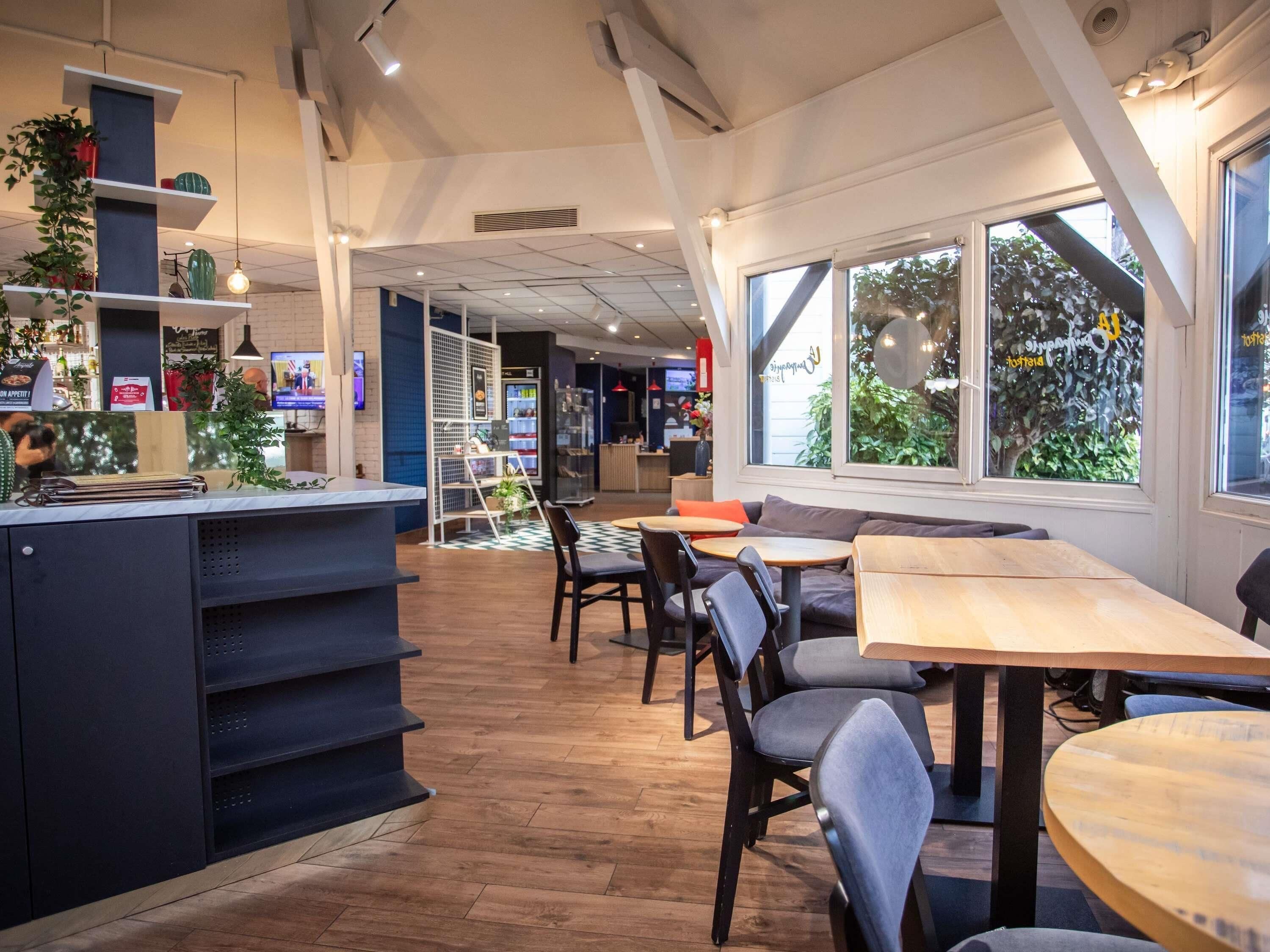 A modern cafe with a counter, seating area, and large windows.
