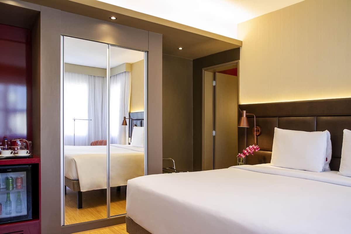 Ein Hotelzimmer mit einem großen Bett, einem Spiegel, einer Minibar und Blick auf ein weiteres Zimmer.