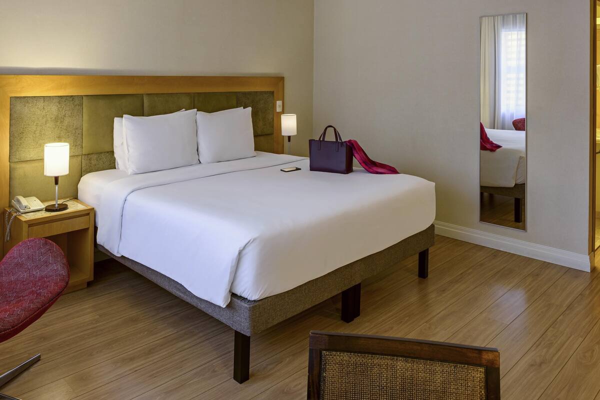 Ein Hotelzimmer mit einem großen Bett, Nachttischlampen, einem Telefon, einer Handtasche und einem Spiegel.