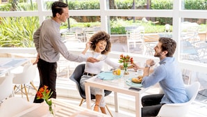Un espace repas lumineux et moderne, doté de grandes fenêtres, de meubles blancs et d’une table dressée pour trois personnes.