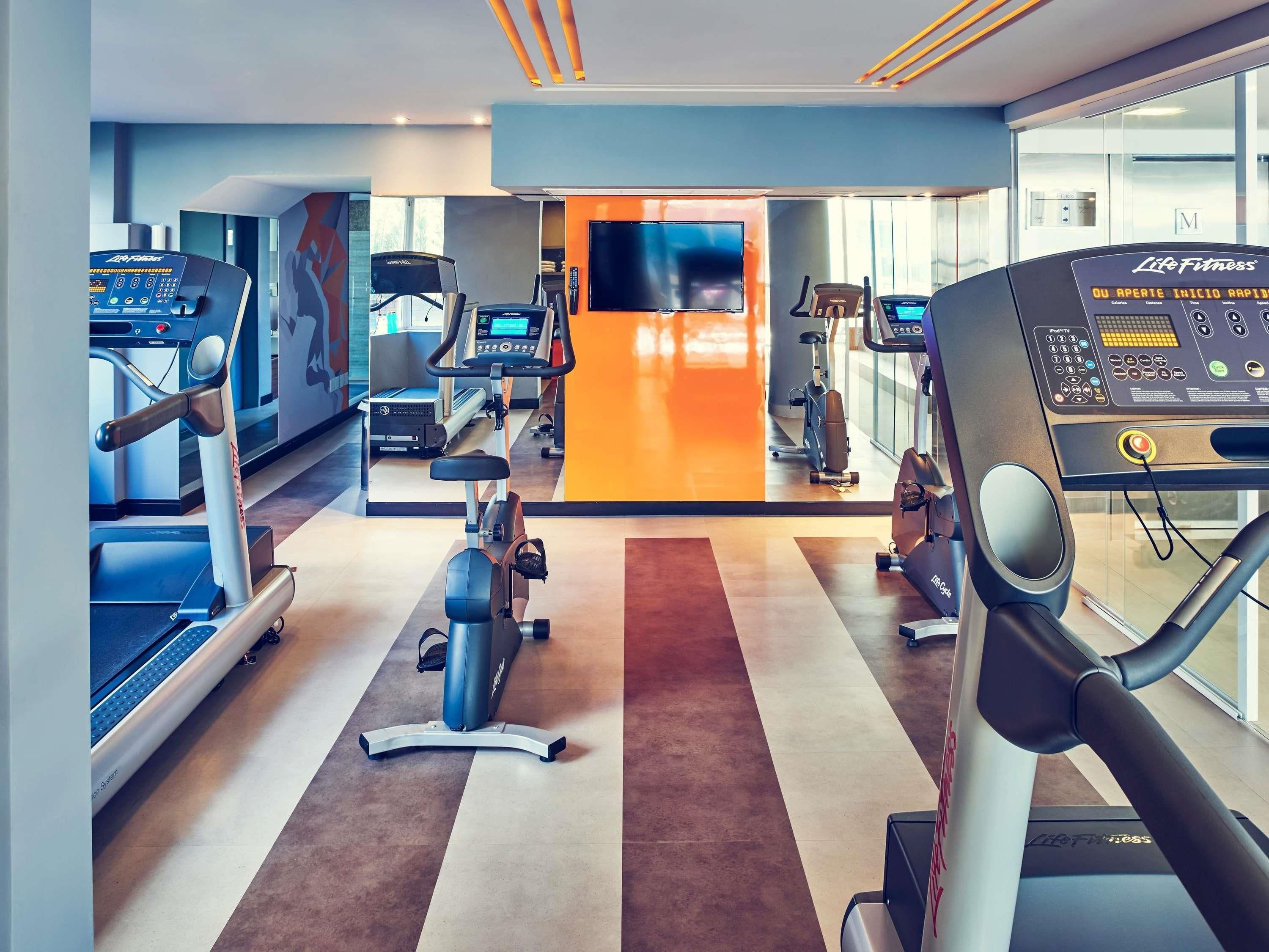 A gym with cardio machines, weight equipment, and a TV screen.