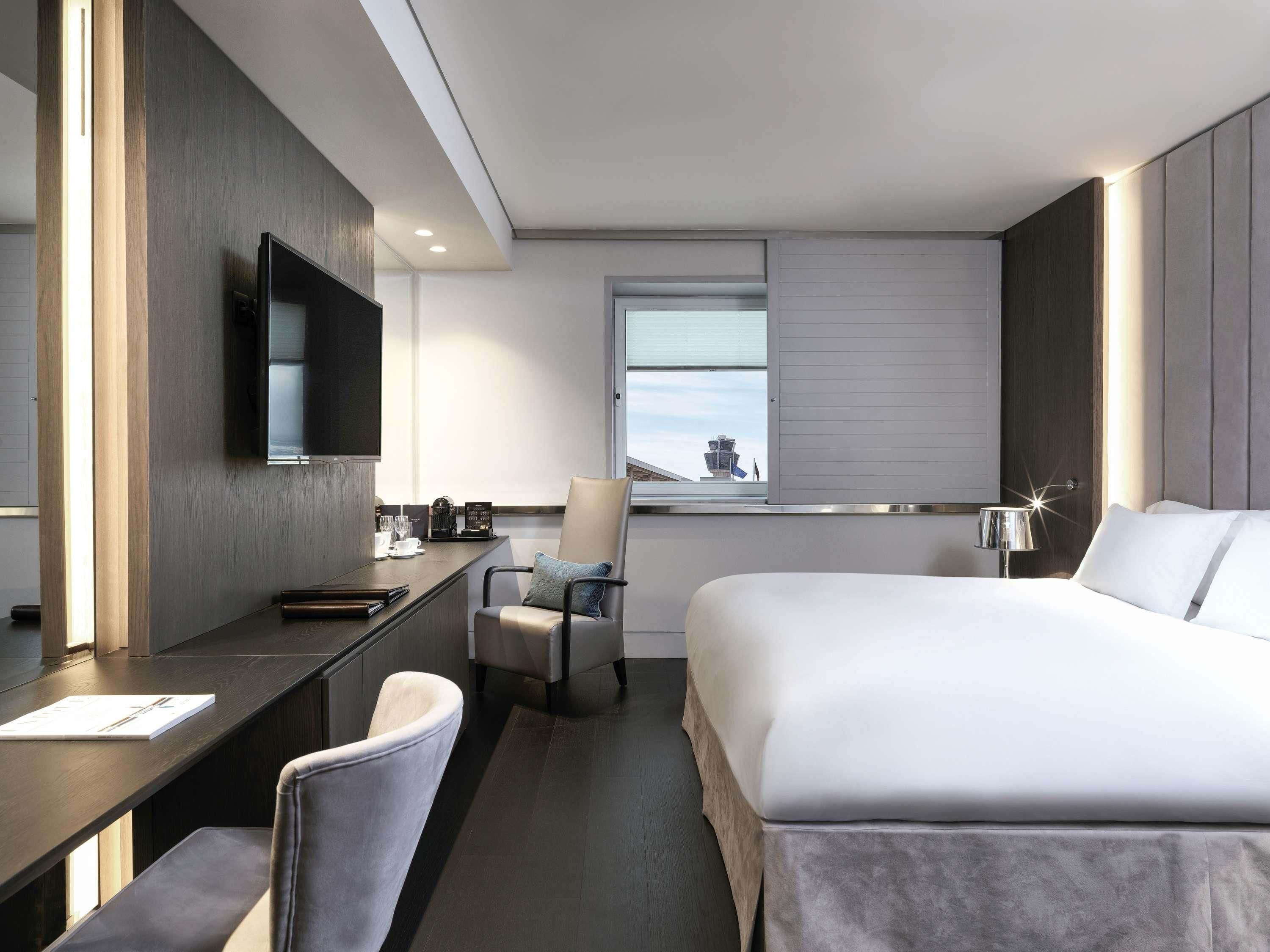 Une chambre d’hôtel moderne équipée d’un lit, d’un bureau, d’une chaise, d’une télévision et d’une fenêtre donnant sur une tour.