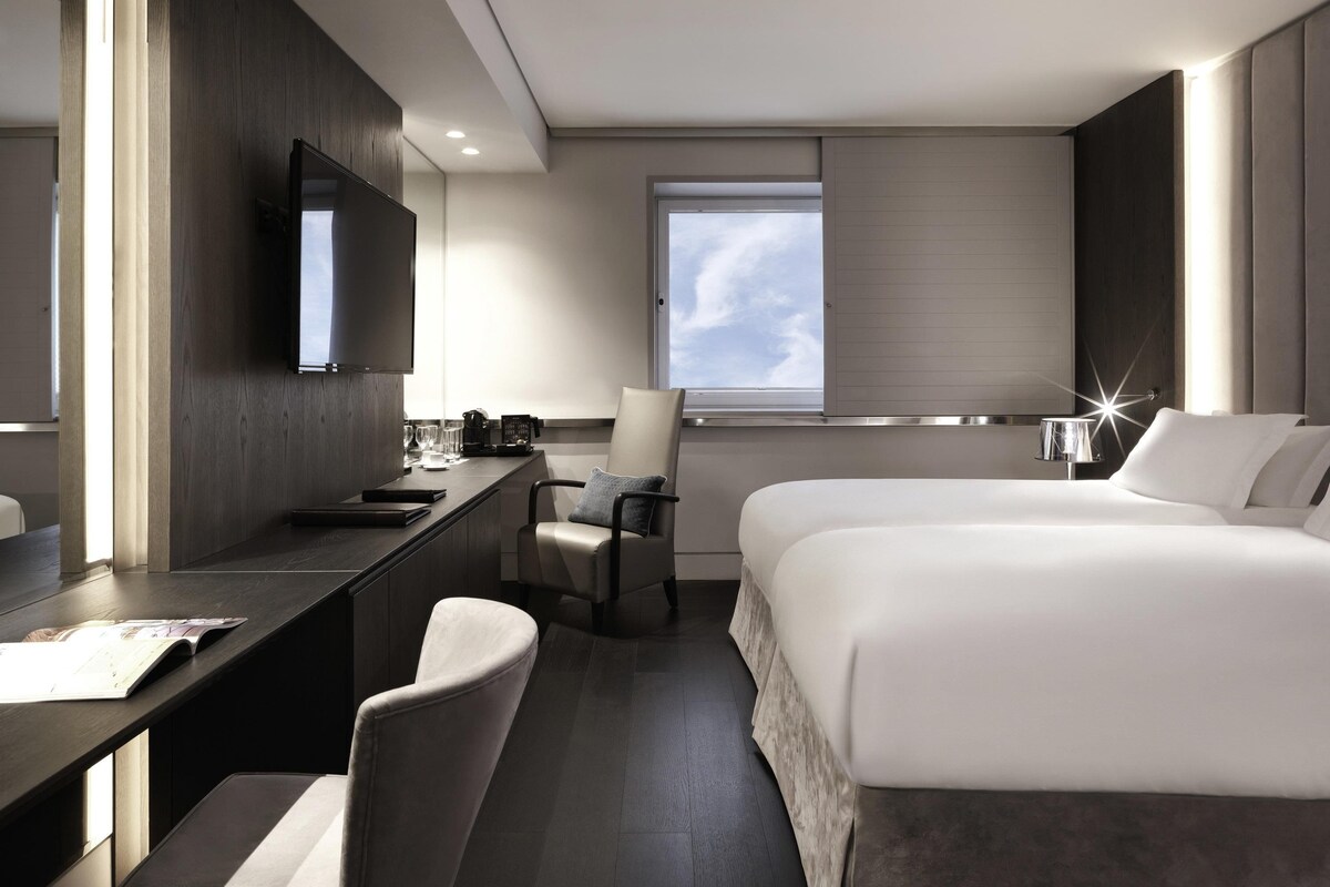Ein modernes Hotelzimmer mit Bett, Schreibtisch, Stuhl, Fernseher und einem Fenster mit Aussicht.
