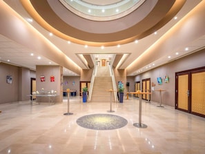 A modern hotel lobby with a central staircase, reception desk, and seating areas.