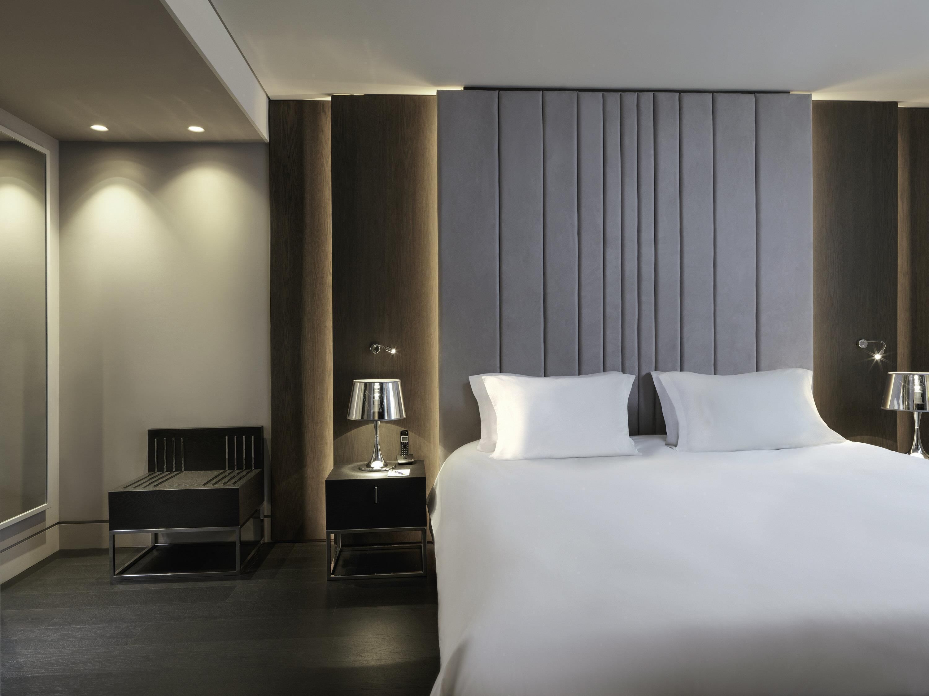 A modern hotel room with a large bed, bedside tables, a nightstand, and a desk.