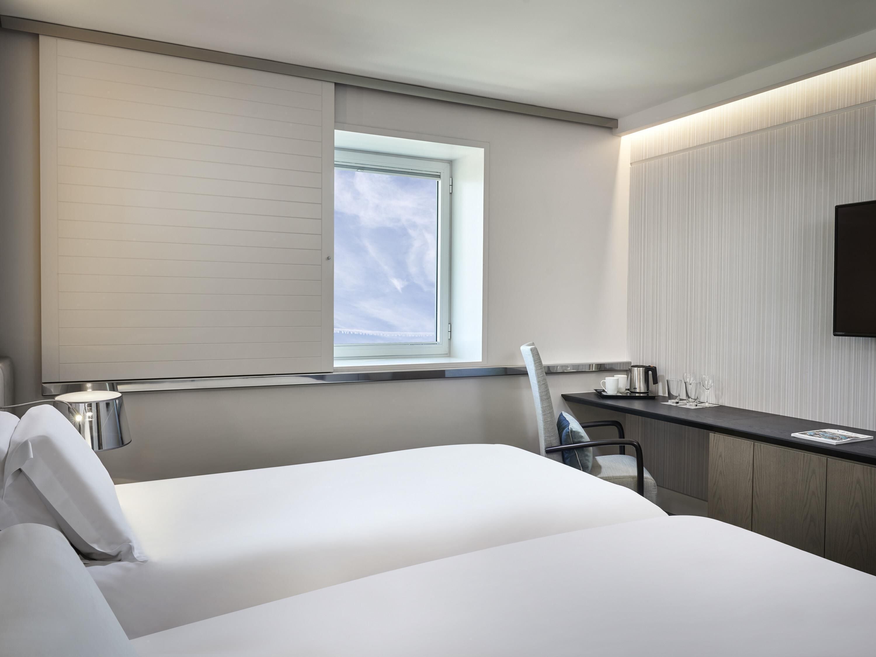 Une chambre d’hôtel moderne équipée d’un lit, d’un bureau, d’une chaise, d’une fenêtre et d’un téléviseur à écran plat.