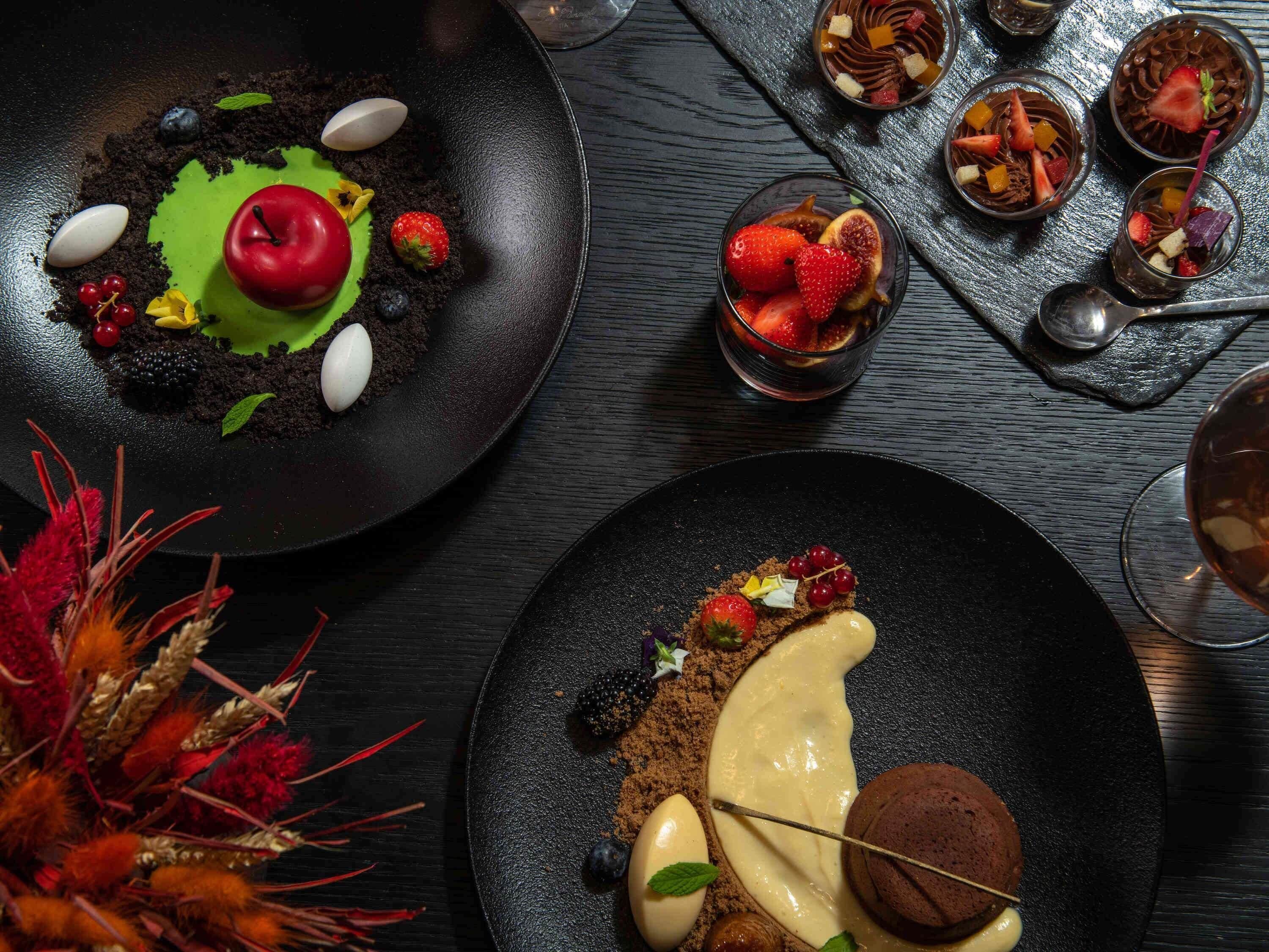 Une présentation de dessert comprenant divers fruits et éléments au chocolat, le tout disposé sur des assiettes noires.