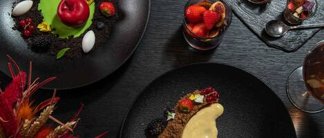Presentación de postres con diversas frutas y detalles de chocolate sobre platos negros.