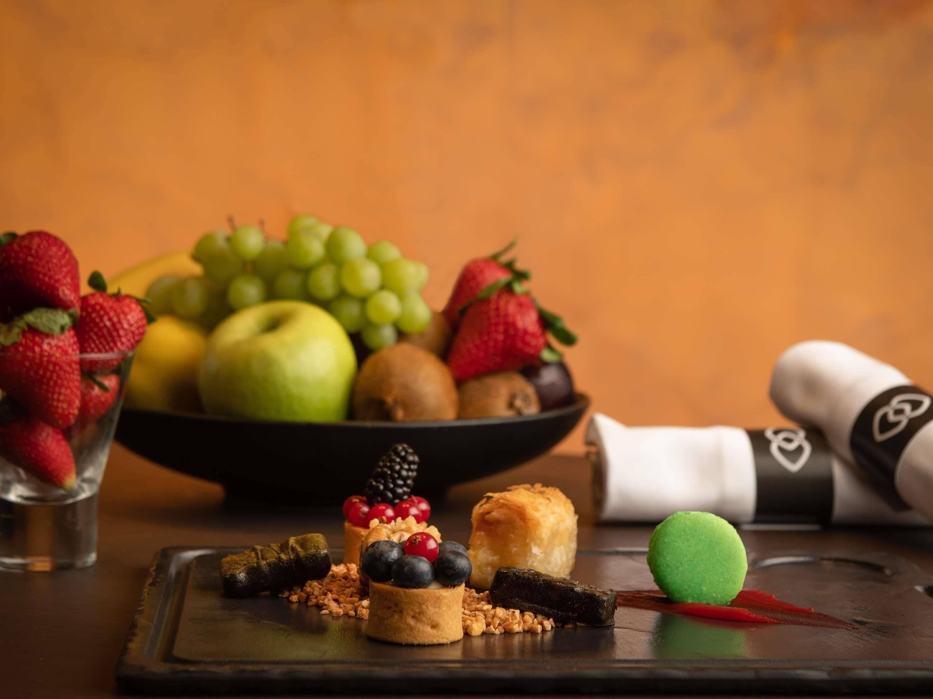 A dessert platter with various fruits and pastries, a bowl of fresh fruits, and a napkin with a heart design.