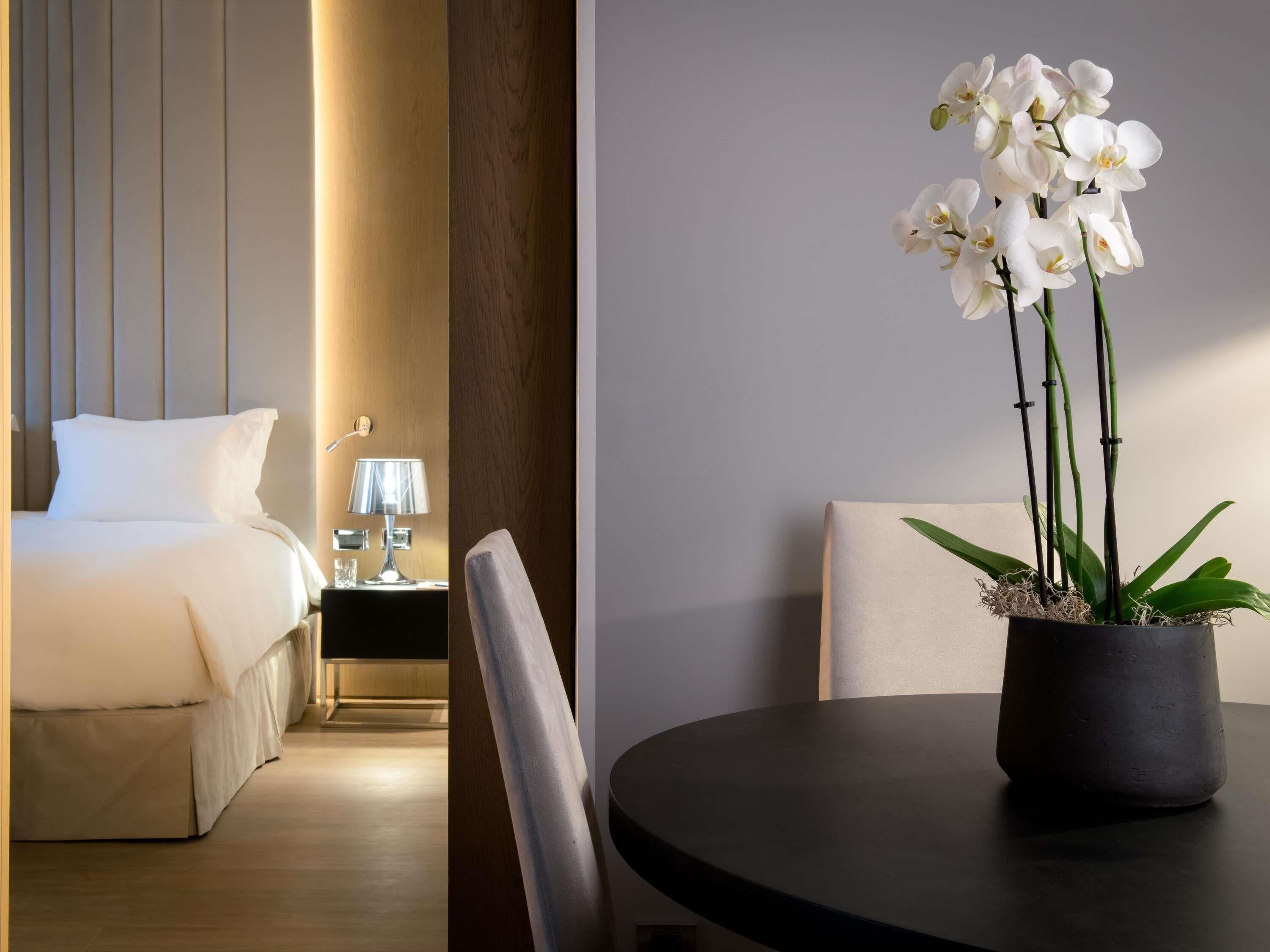Et hotelværelse med en seng, et sengebord, en lampe og en orkidé i potte.
