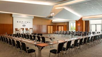 Ein Konferenzraum mit langem Tisch, Stühlen und einer Präsentationsleinwand im Sofitel Athens Airport.