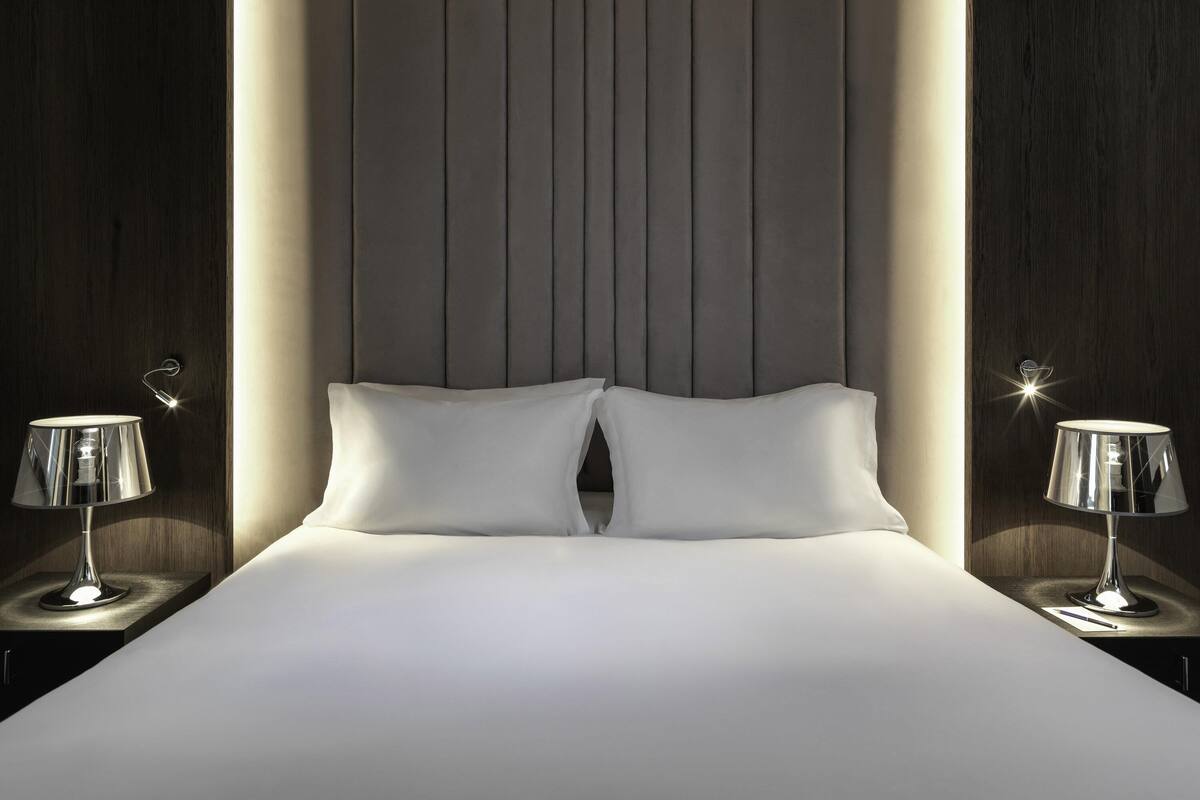 A modern bedroom with a large bed, two bedside lamps, and a headboard with vertical lines.