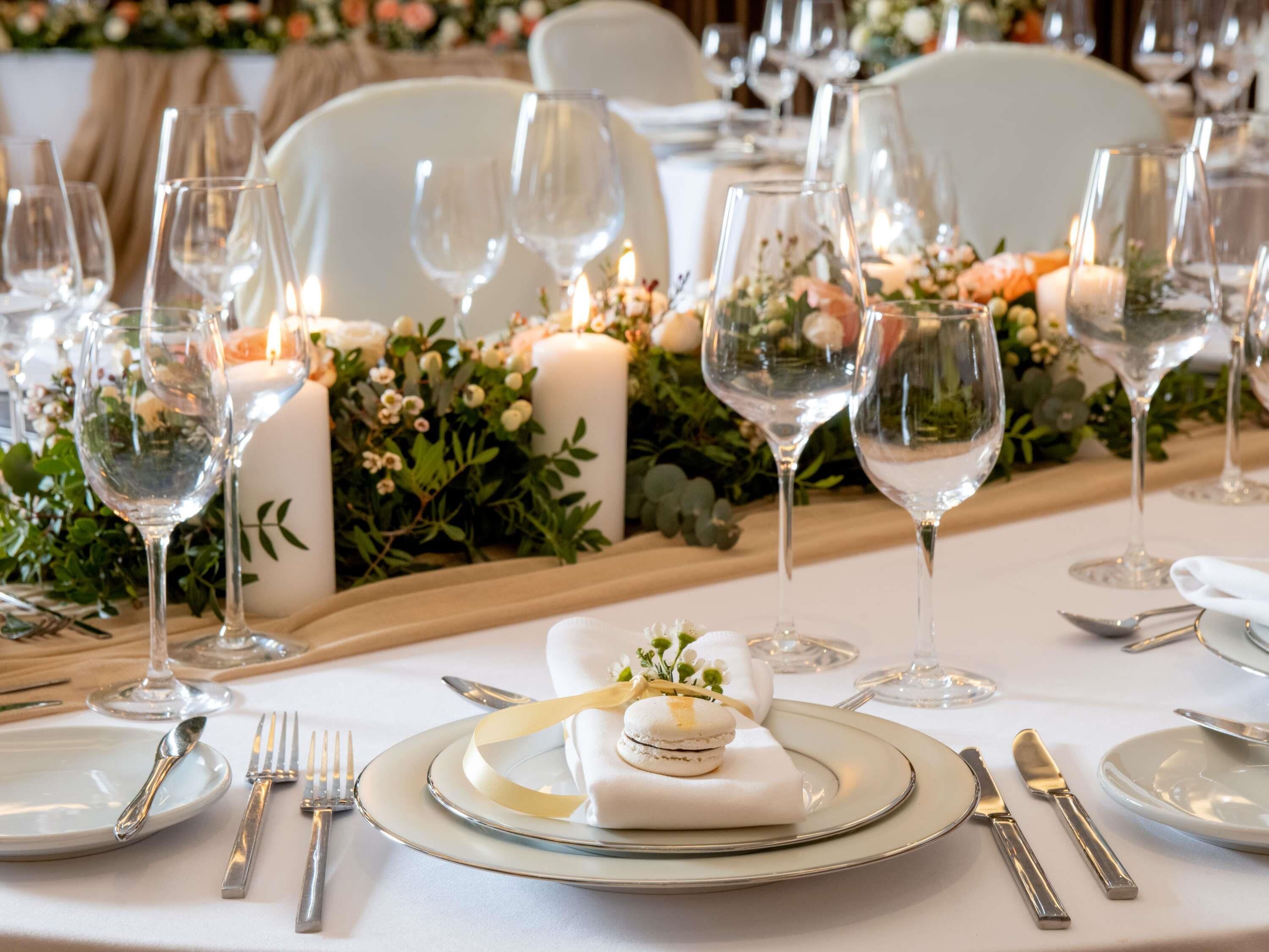 Mesa dispuesta para un evento formal con platos blancos, cubiertos y copas de vino, rodeada de velas y adornos florales.