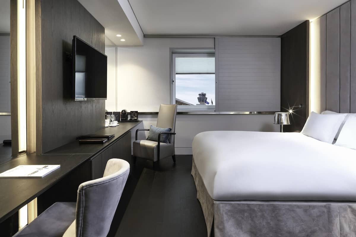 A hotel room with a bed, desk, chair, and a TV mounted on the wall.