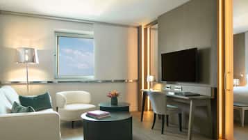 Una habitación de hotel moderna con sofá, escritorio, silla, televisor y ventana con persianas.