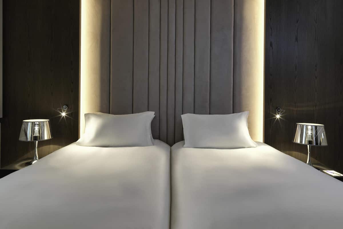 A double bed with a padded headboard, two bedside lamps, and a neutral-toned wall.