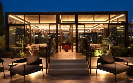 A modern building with a glass facade, outdoor seating area, and a staircase leading to the entrance.