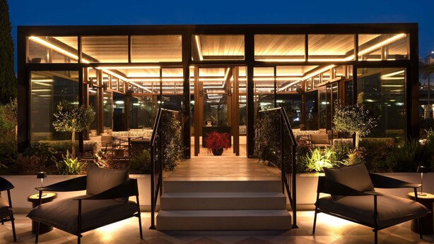 A modern building with a glass facade, outdoor seating area, and a staircase leading to the entrance.