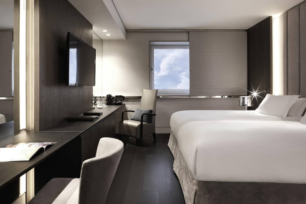 A modern hotel room with a bed, desk, chair, TV, and a window with a view.