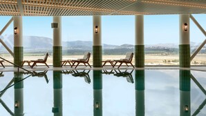 An indoor swimming pool with lounge chairs and a view of mountains.