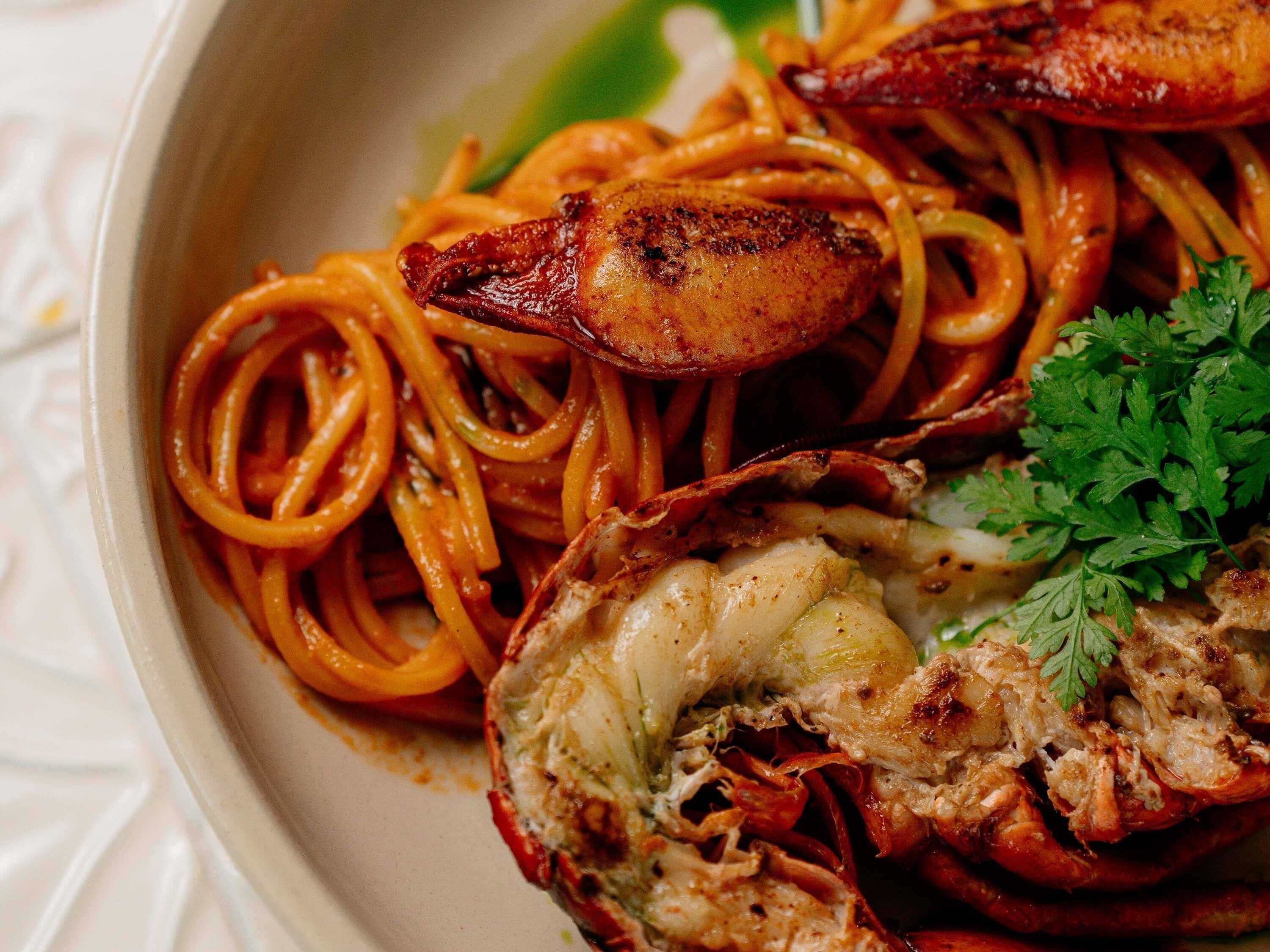 A plate of spaghetti with a lobster tail and a garnish of parsley.