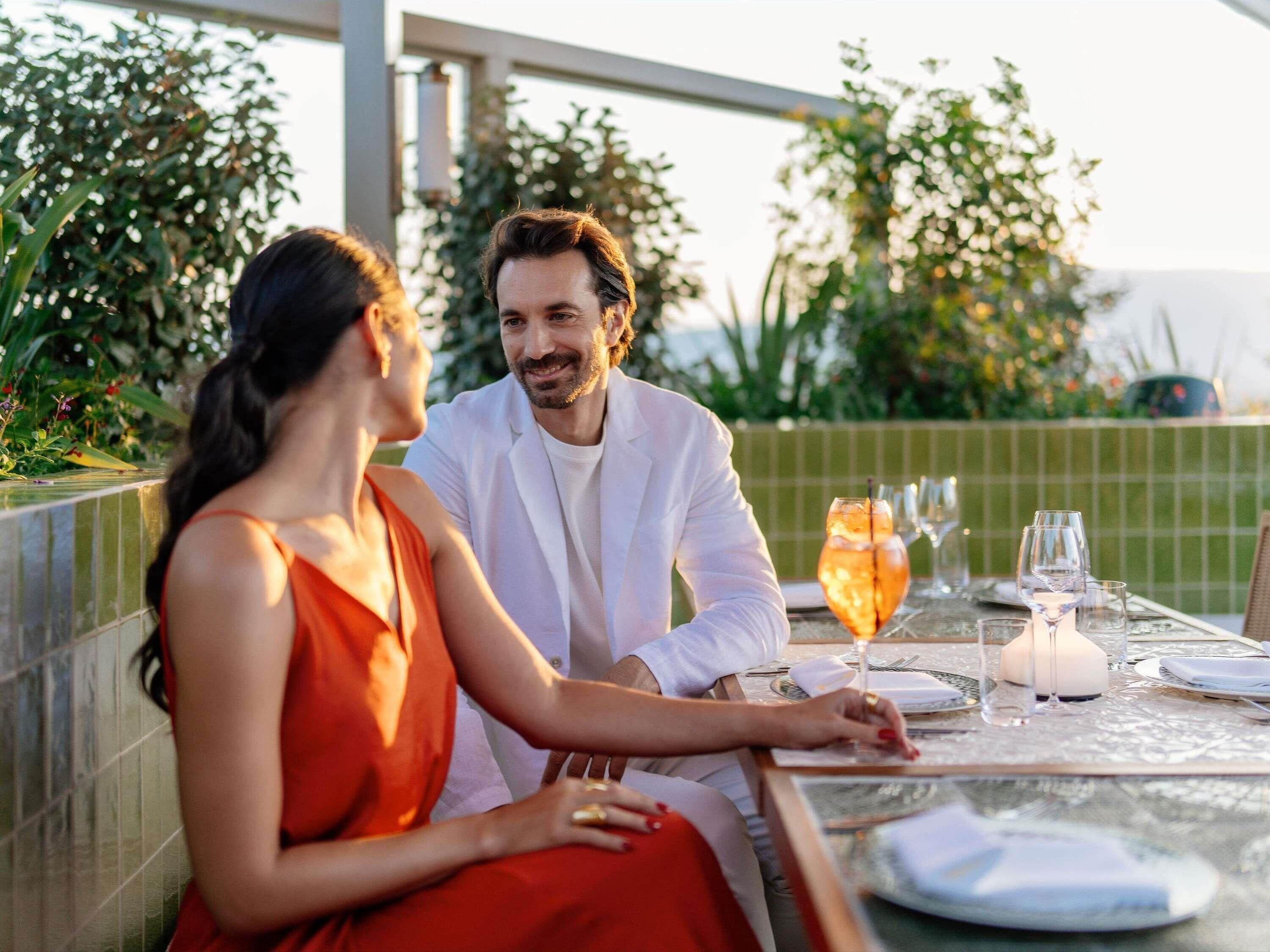 A couple dining at an outdoor table with a view of greenery and a tiled wall.