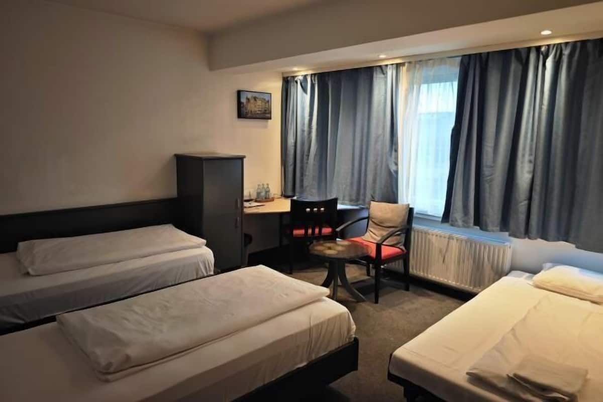 Habitación de hotel con dos camas, un escritorio, una silla y un radiador.