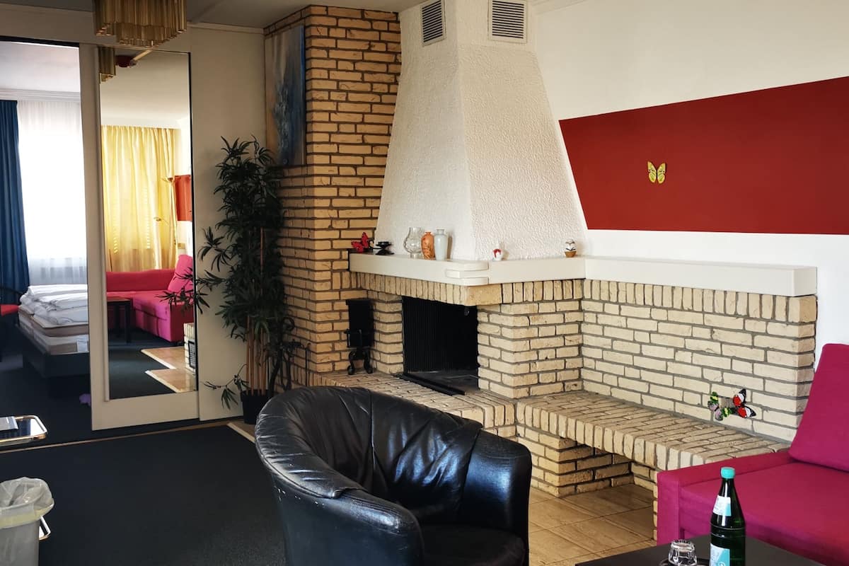 Una sala de estar con chimenea de ladrillo, un sofá de cuero, un sofá rojo y una mesa de comedor con una botella y una copa.
