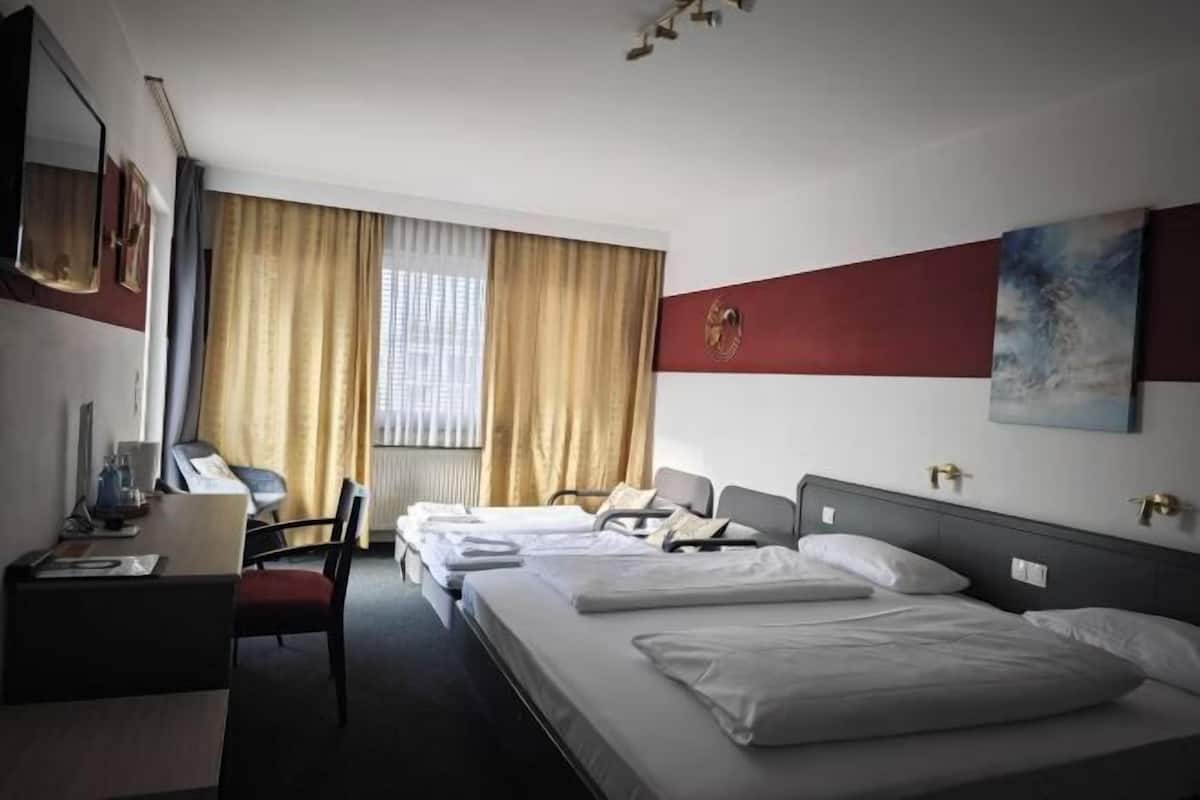 Habitación de hotel con escritorio, dos camas, una silla, ventana con cortinas y un cuadro en la pared.