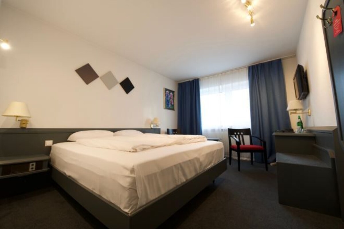 A hotel room with a bed, a desk, a chair, and a TV.