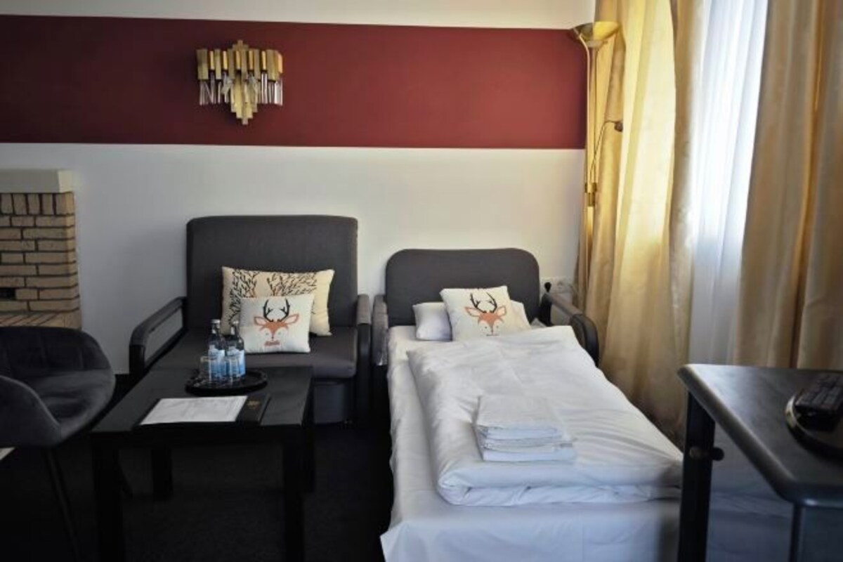 A hotel room with a bed, two armchairs, a small table with a tray of bottled water, a brick-patterned wall, and a red and white color scheme.