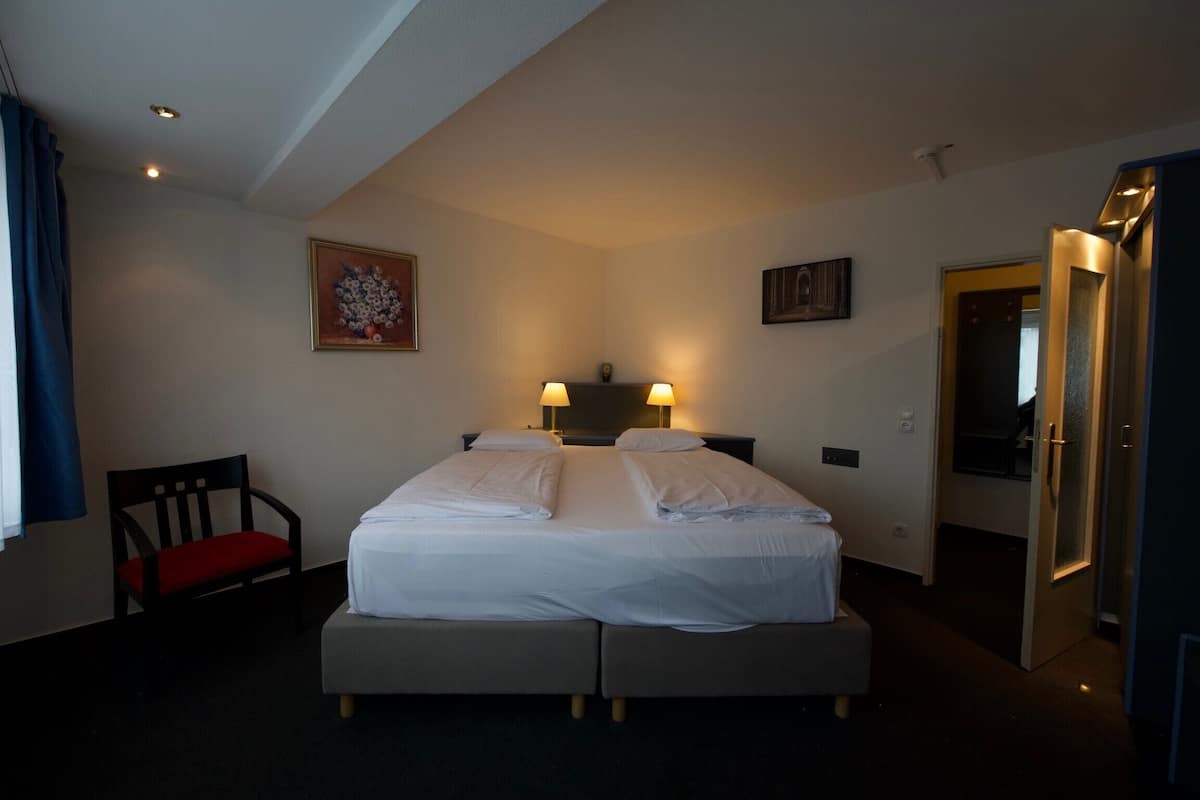 Una habitación de hotel con una cama doble, dos lámparas de noche, una silla y un cuadro en la pared.