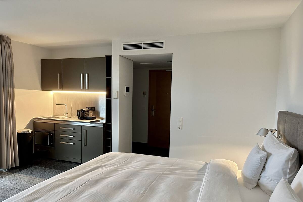 A hotel room with a bed, a kitchenette, and a bathroom.