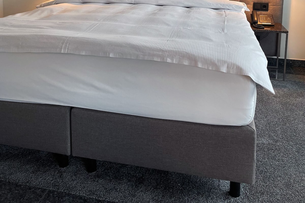 A hotel room with a large bed, two bedside lamps, a phone on a side table, and a carpeted floor.