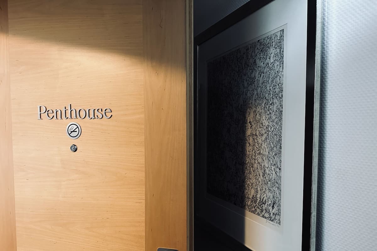 A wooden door labeled "Penthouse" with a no-smoking sign, a keyhole, and a framed artwork on the adjacent wall.