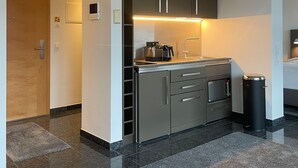 Una cocina moderna con electrodomésticos de acero inoxidable, horno empotrado y microondas. Hay un cubo de basura y una pequeña superficie de encimera con una cafetera.