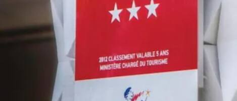 A red and white award plaque with the letter "H" and three stars, indicating a 5-year award from the French Ministry of Tourism.