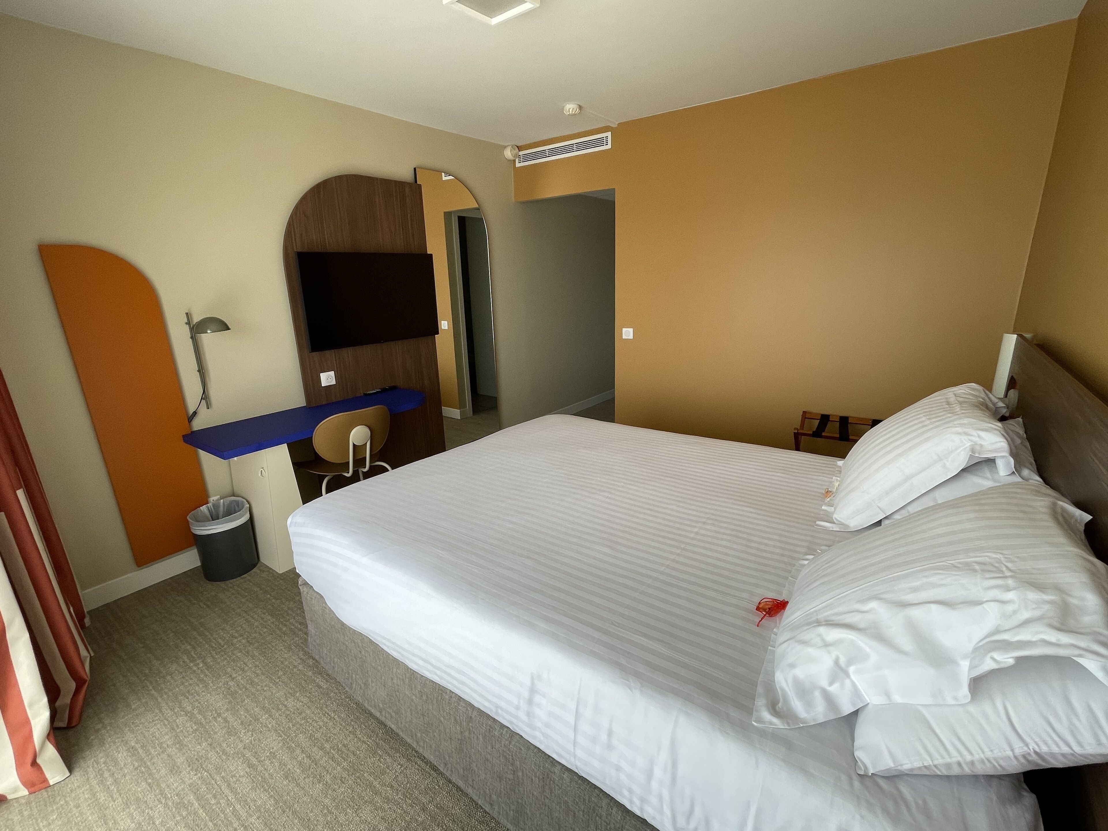 Habitación de hotel con una cama grande, un escritorio, una silla, un televisor y un cesto de basura.