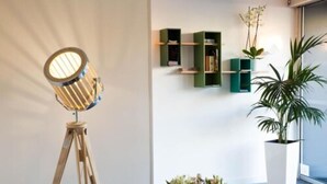 A modern room with a tripod floor lamp, green shelving units, a potted plant, and a vase of flowers. - Hotel Abrial by Soniho (Cannes)