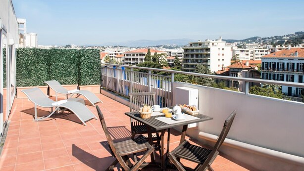 A balcony with a table set for breakfast, sun loungers, and a view of the cityscape. - Hotel Abrial by Soniho (Cannes)