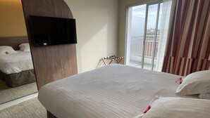 A hotel room with a large bed, a TV mounted on the wall, and a view of the city through the window. - Hotel Abrial by Soniho (Cannes)
