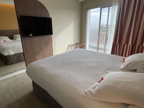 Habitación de hotel con una cama grande, un televisor montado en la pared y vistas de la ciudad a través de la ventana.