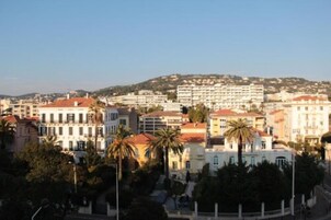 Un paysage urbain côtier mêlant des immeubles résidentiels et commerciaux, dont un bâtiment blanc imposant surmonté d’un toit rouge, et plusieurs palmiers au premier plan.
