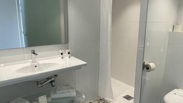 Een badkamer met een wit wastafelmeubel, spiegel, douche en toilet.