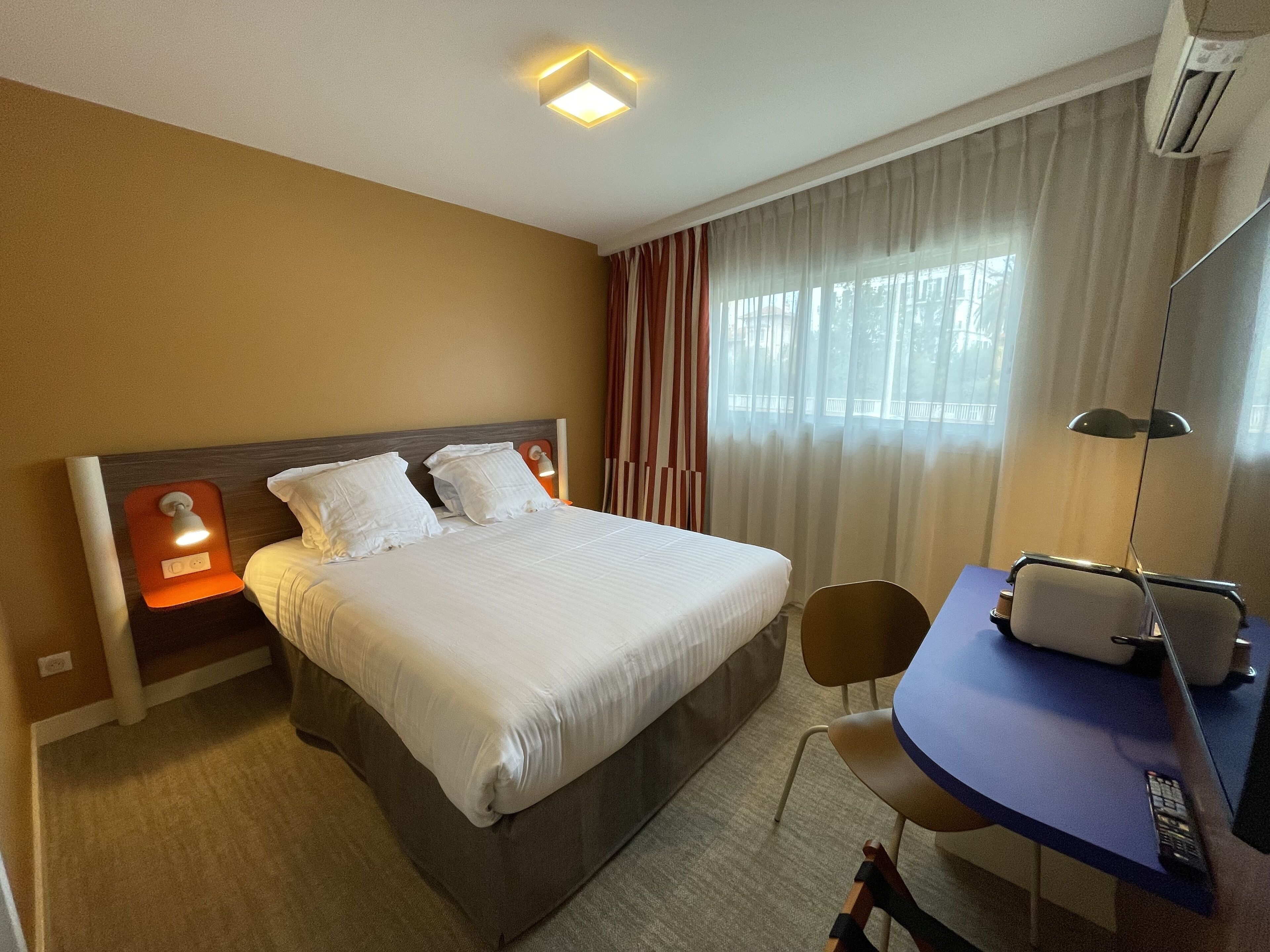 Una camera d'albergo con un letto, una scrivania, una sedia e una finestra con tende.