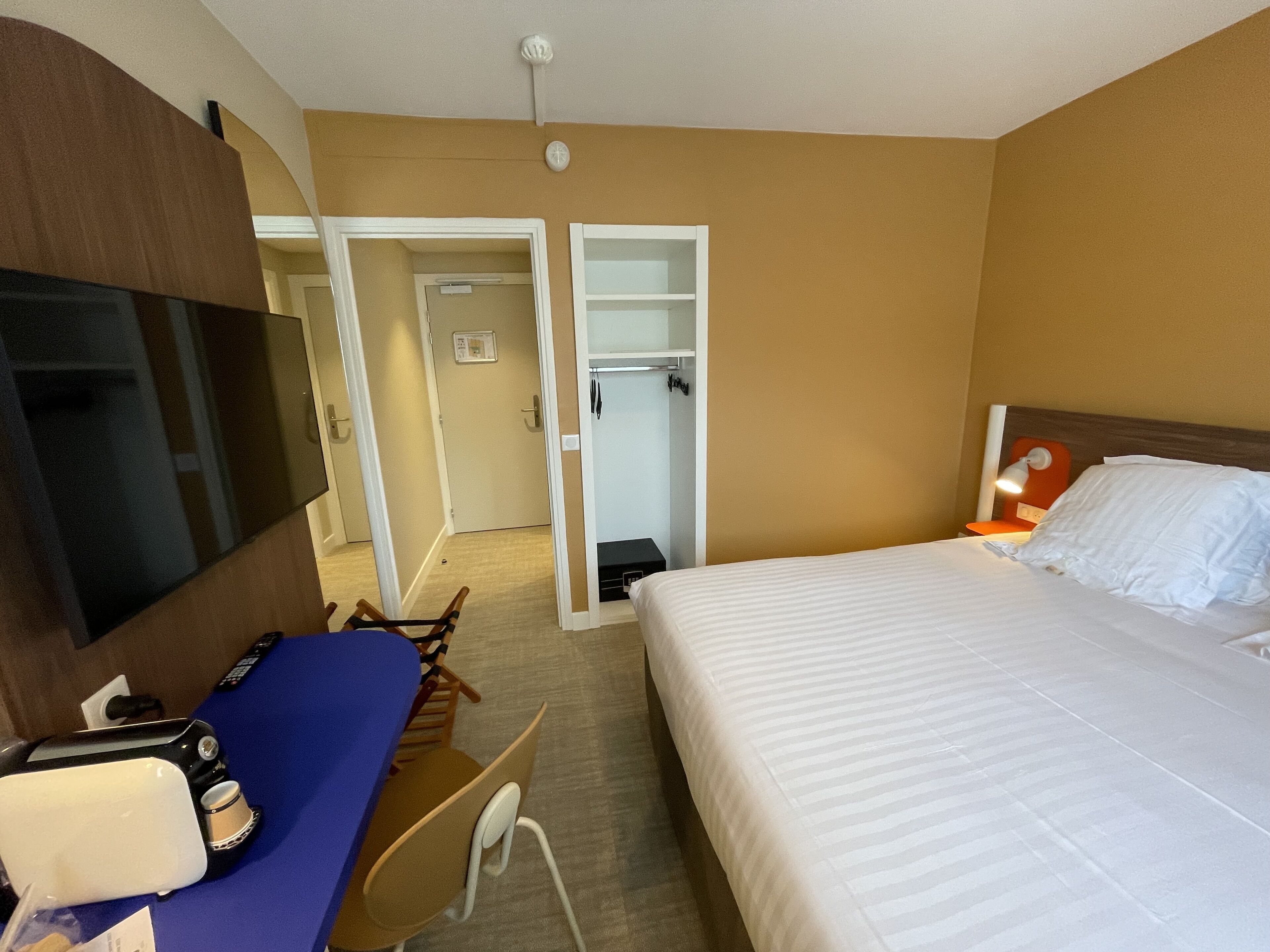 A hotel room with a bed, a desk with a computer, a TV, and a wardrobe.
