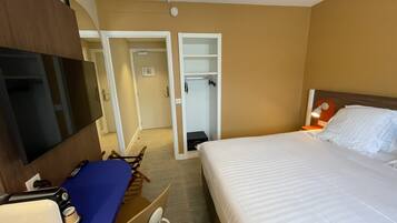 A hotel room with a bed, a desk with a computer, a TV, and a wardrobe.