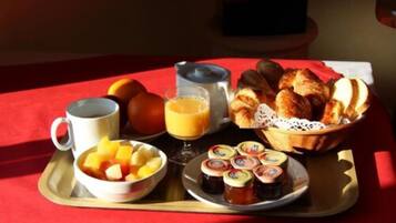 Ein Frühstücksbrett mit Früchten, Saft, Croissants und Marmelade auf einer roten Tischdecke.