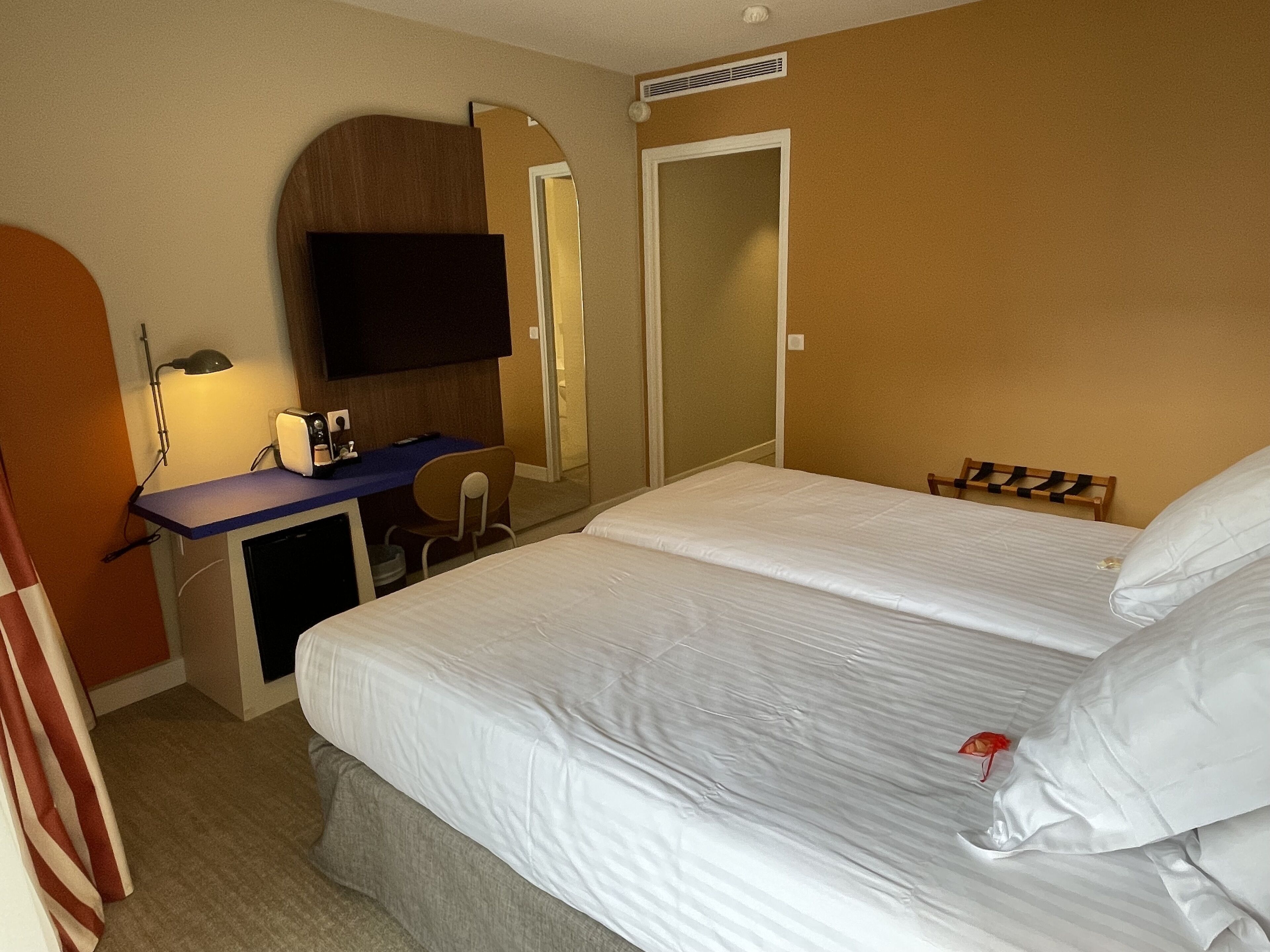 Una habitación de hotel con cama, escritorio con silla, televisor y espejo.