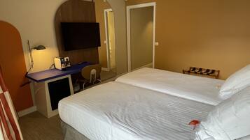Una habitación de hotel con cama, escritorio con silla, televisor y espejo.